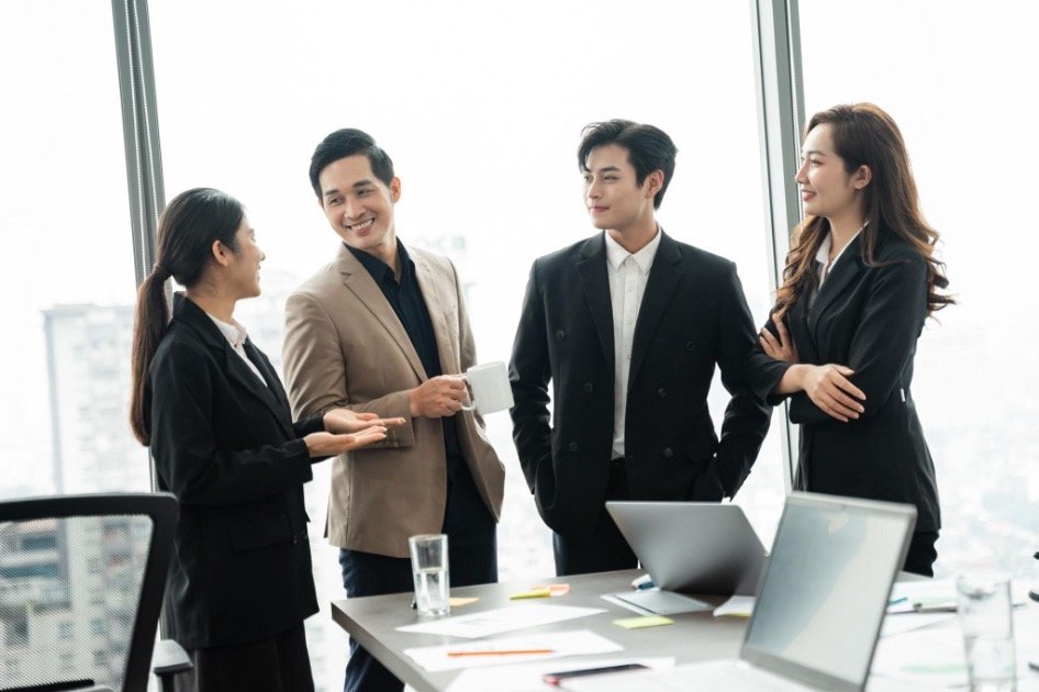 Four young Vietnamese business professionals in a modern Ho Chi Minh City office, smiling during a relaxed conversation around the meeting table.