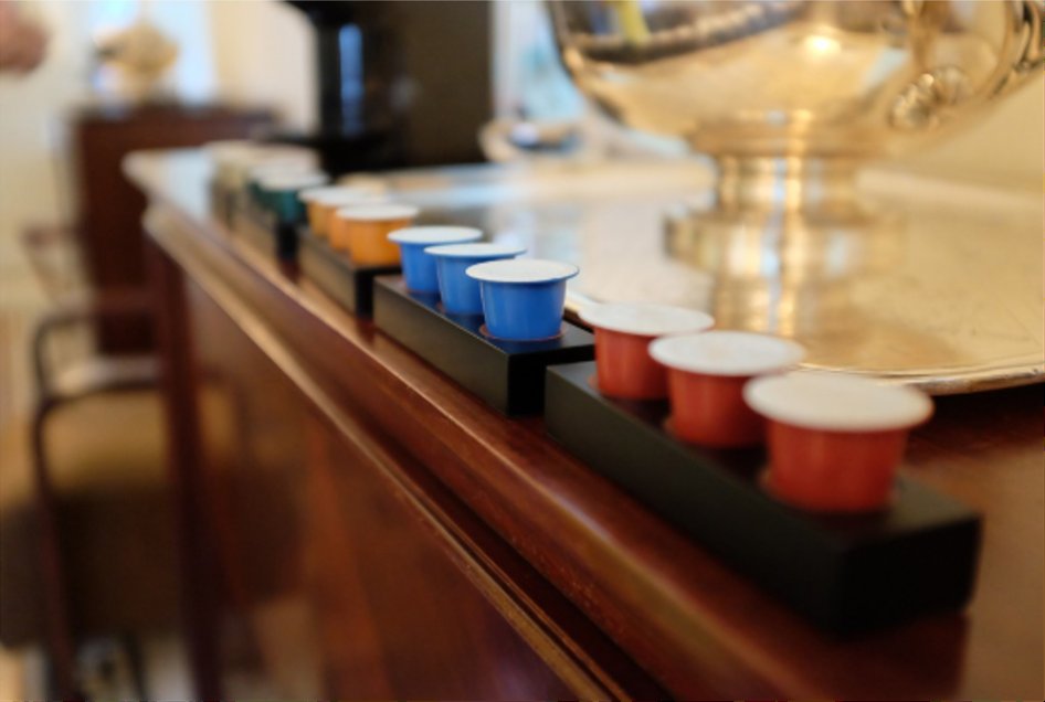 Row of Le Caïffa colored capsules displayed on an elegant wooden bar counter in an upscale hotel setting with a silver samovar in the background.