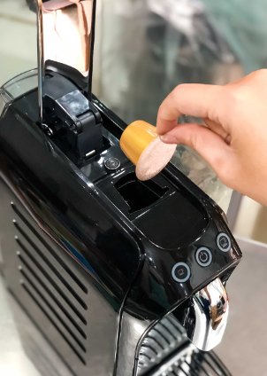 A hand loading a Le Caïffa capsule into a Nespresso-compatible espresso machine.