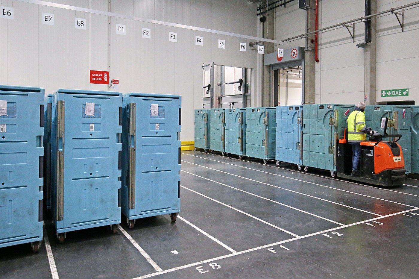 Olivo Cold Logistics insulated containers lined up on a warehouse floor at the Colruyt distribution centre, with an operator on an electric pallet truck.