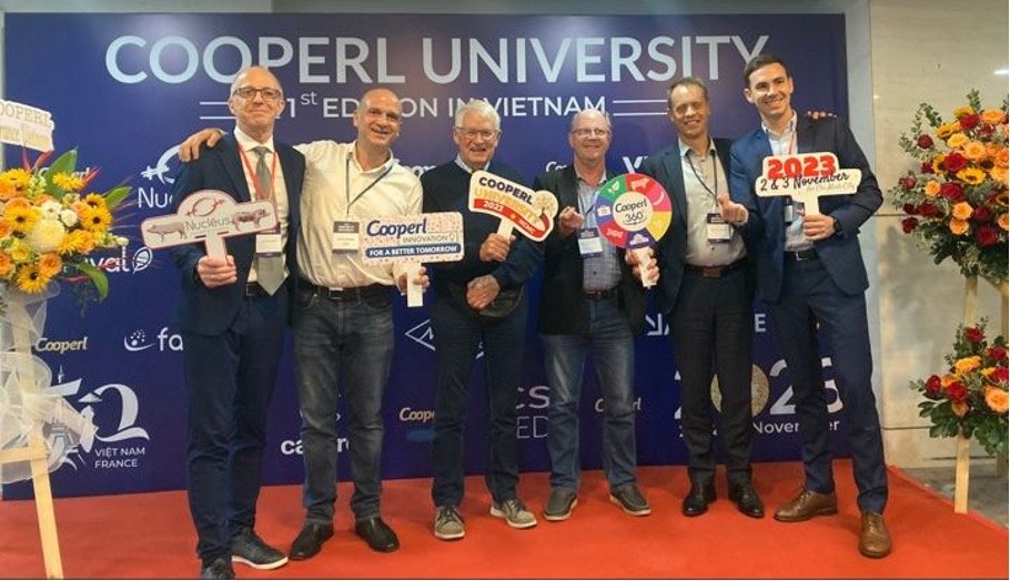 Group photo of six men including Vincent Treluyer on a red carpet in front of a Cooperl University 1st edition in Vietnam step-and-repeat backdrop, each holding a Cooperl-branded paddle sign, Ho Chi Minh City, November 2023.