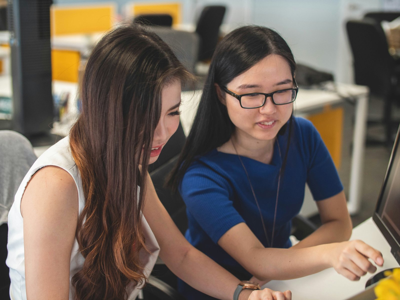 Two young Asian professionals working together at a computer in a modern Vietnamese open-plan office, illustrating team collaboration and skill development.